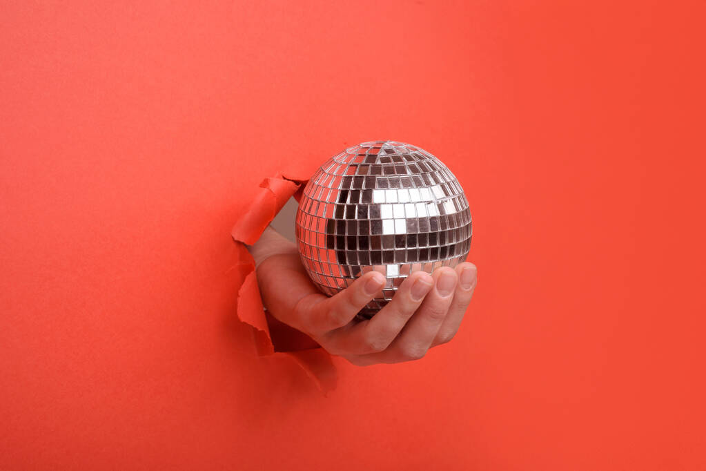 Main tenant Silver boule miroir disco sur le mur de papier rouge déchiré. Espace de copie réservé à votre publicité et à votre contenu d'offre ou de vente
. - Photo, image