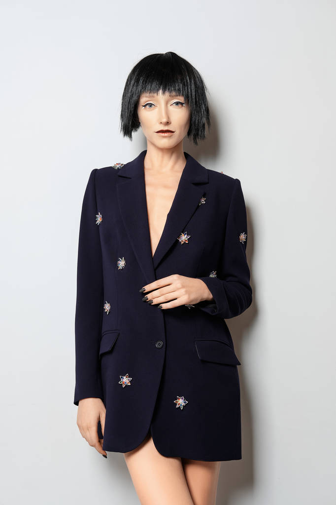 Fashion model met zwarte bob kapsel poseren in de buurt van de muur in blauwe jas met edelstenen decor - Foto, afbeelding