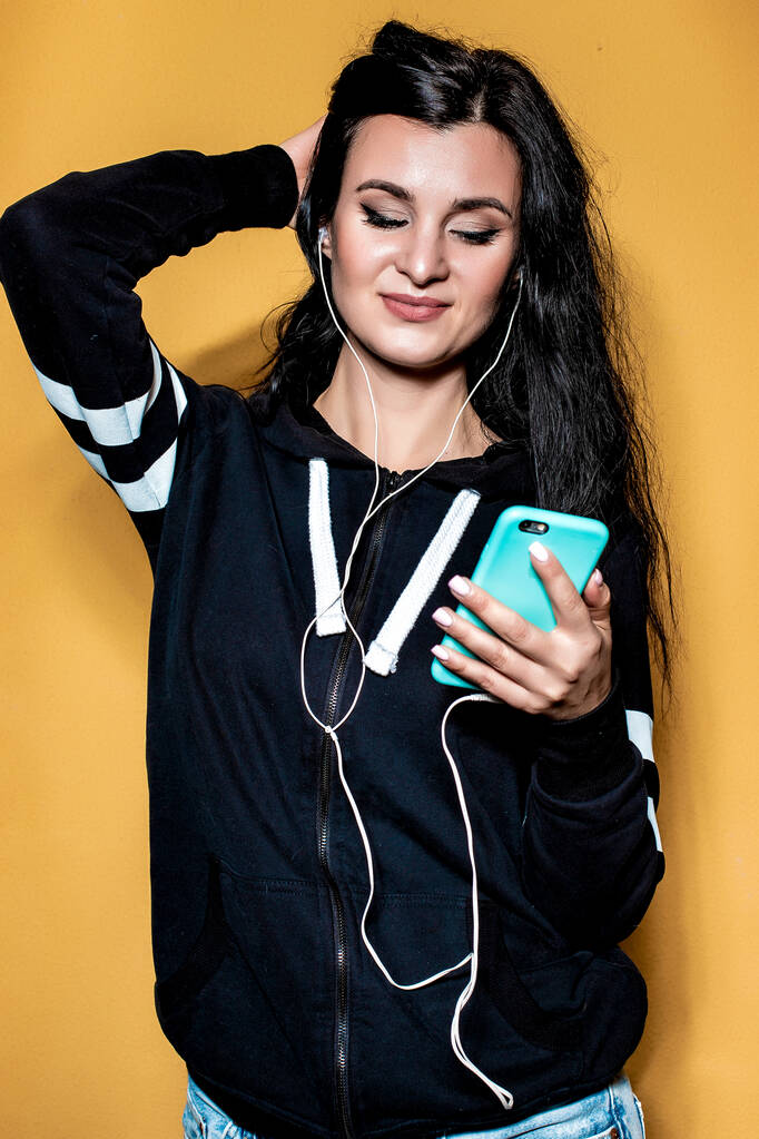 Portret van een mooi brunette meisje, op een oranje achtergrond in een fiets en jeans, die luistert naar muziek - Foto, afbeelding