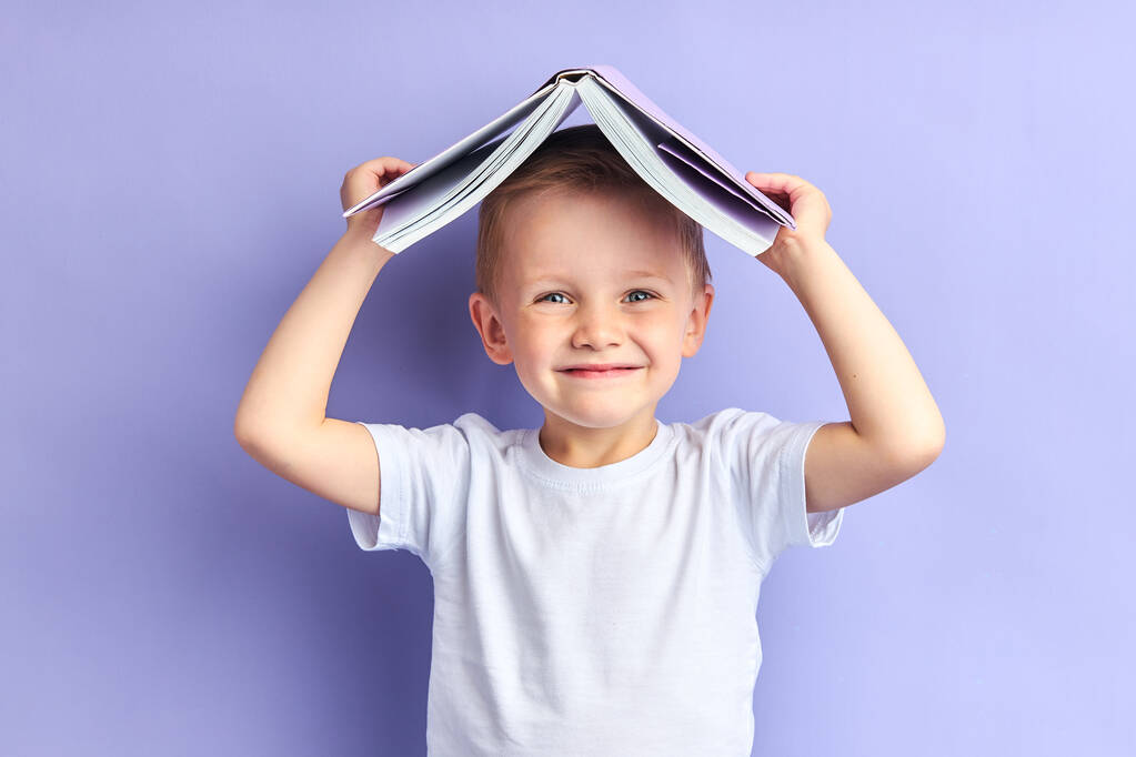 Zabawny chłopiec trzyma książkę nad głową - Zdjęcie, obraz