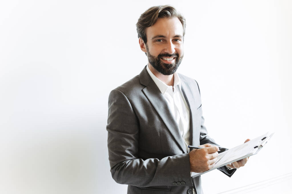 Képek mosolygós sikeres üzletemberről, aki írótáblát tart és jegyzeteket ír le, miközben az irodában dolgozik - Fotó, kép