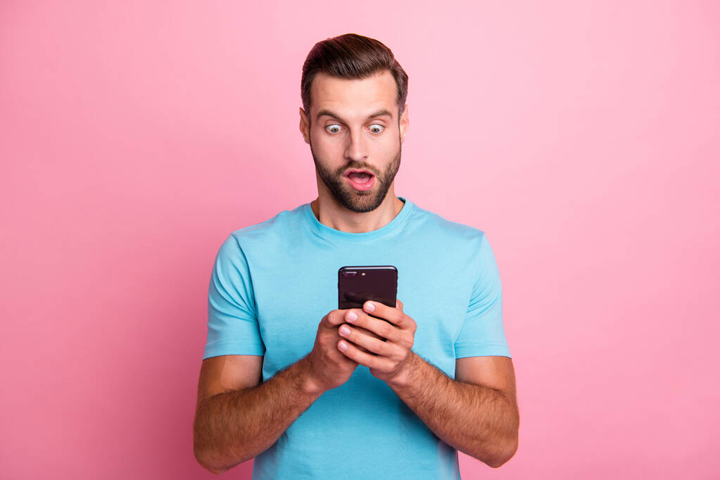 Photo of casual astonished crazy grimacing man scared of message received looking into screen information about being fired isolated pastel color background in blue t-shirt - Photo, Image
