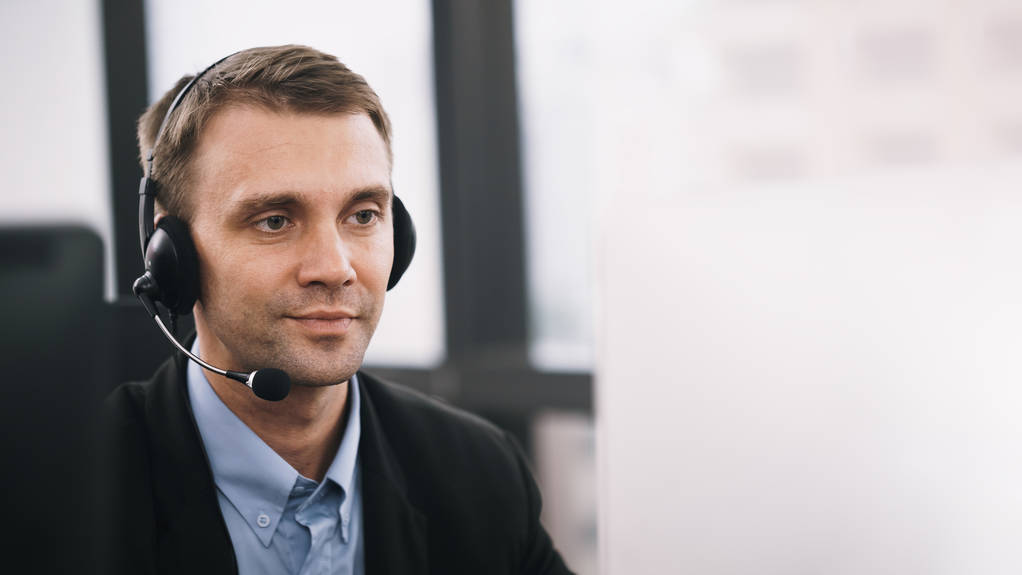Hymyilevä komea mies istuu asiakaspalvelun toimistossa kuulokkeet työskentelevät call center
 - Valokuva, kuva