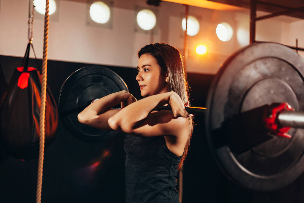 Мышечная женщина в спортзале делает тяжелые упражнения веса. Молодая женщина занимается тяжелой атлетикой в оздоровительном клубе
 - Фото, изображение