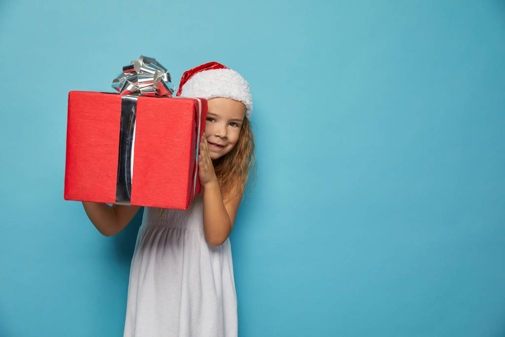  Κορίτσι σε Σάντα κόκκινο καπέλο κρατώντας χριστουγεννιάτικο δώρο - Φωτογραφία, εικόνα