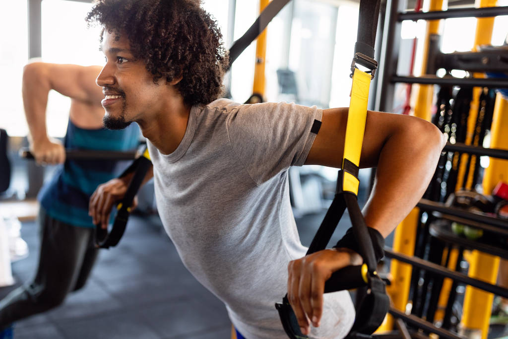 Man doet push-ups training met trx fitness riemen in de sportschool. Workout gezonde levensstijl sport concept - Foto, afbeelding