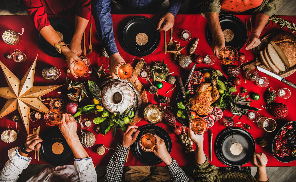 Arkadaşların ailesi Noel 'i ya da yeni yılı kutluyor. Kırmızı masa örtüsü, köpüklü şarap, kızarmış hindi ya da tavuk, tatlı kek, mevsimlik meyve ve renkli dekorasyonlarla ziyafet çeken insanların olduğu düz bir masa. Kış - Fotoğraf, Görsel