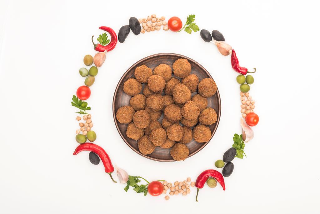 vista superior de grão de bico, alho, tomate cereja, salsa, azeitonas, pimenta, cebola verde dispostas em armação redonda em torno de bolas de falafel na placa isolada em branco
 - Foto, Imagem