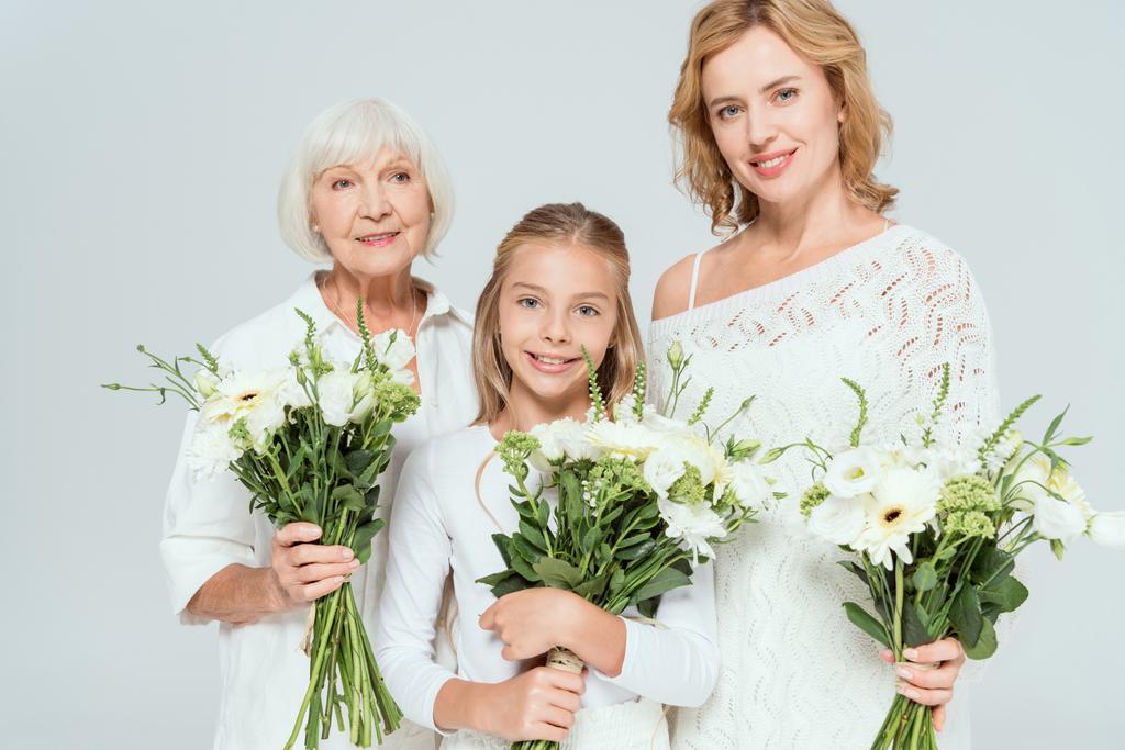Lächelnde Enkelin, Mutter und Großmutter mit Blumensträußen in grau  - Foto, Bild