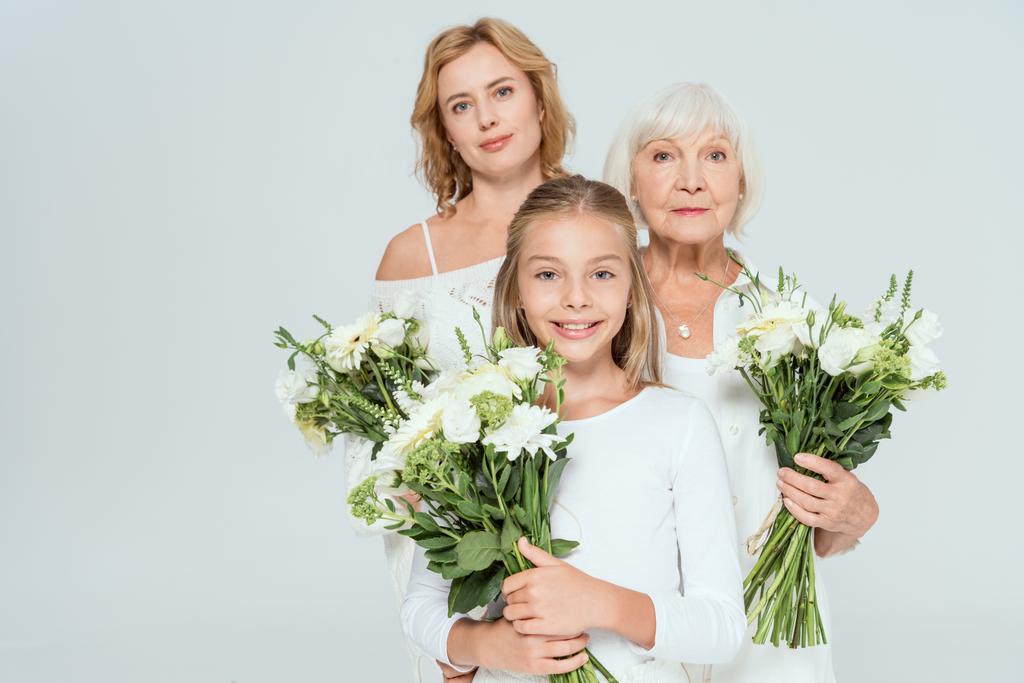 Lächelnde Enkelin, Mutter und Großmutter mit Blumensträußen in grau  - Foto, Bild