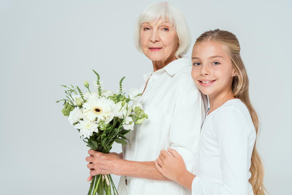 nieta sonriente abrazando a la abuela con ramo aislado en gris
  - Foto, Imagen