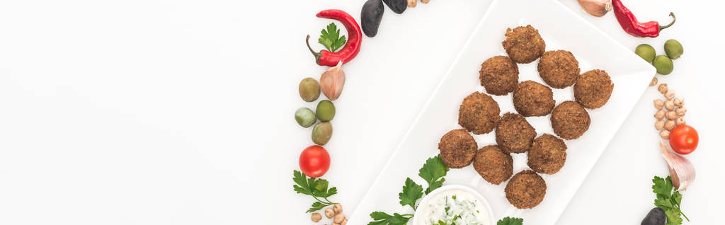 вид сверху овощей, расположенных в круглой рамке вокруг фалафеля на тарелке с соусом на белом фоне, панорамный снимок
 - Фото, изображение