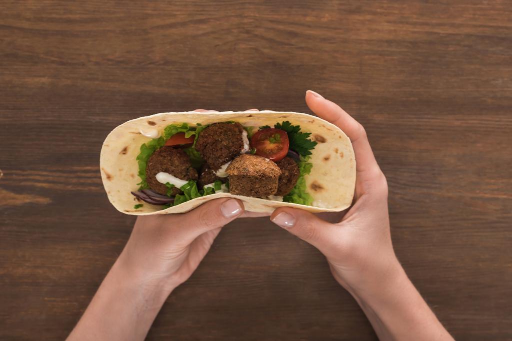 cropped view of woman holding falafel with vegetables and sauce in pita on wooden table - Photo, Image