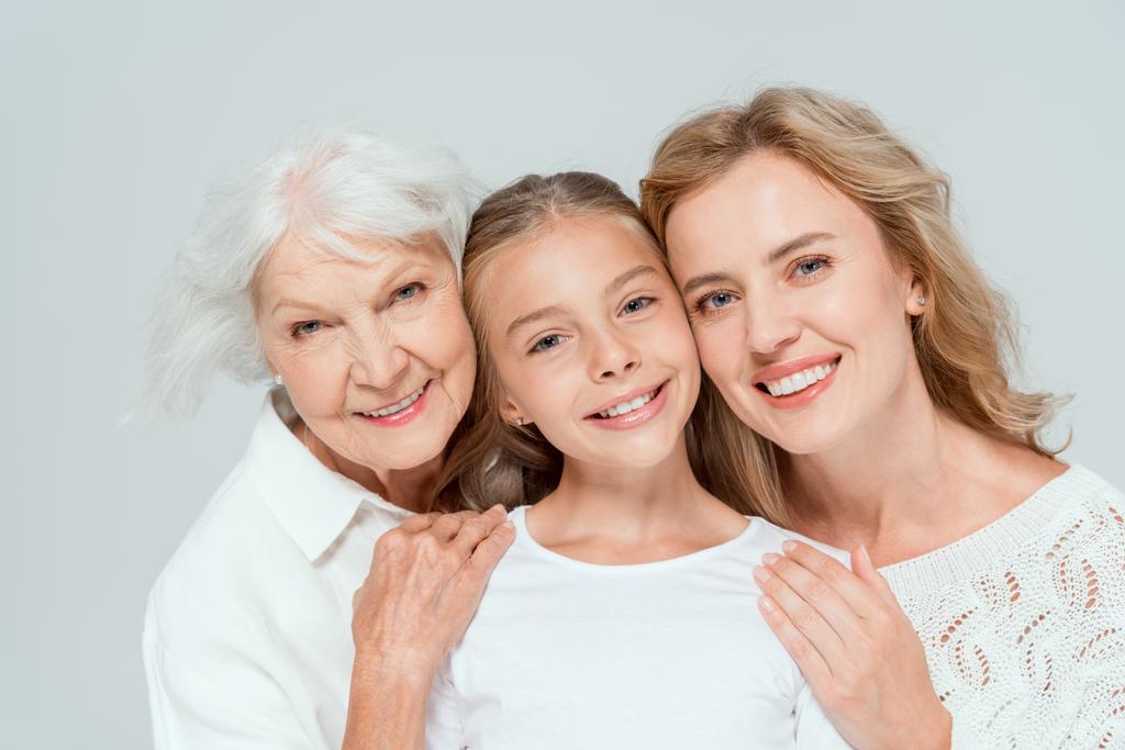 glimlachende moeder en oma knuffelen kleindochter geïsoleerd op grijs  - Foto, afbeelding