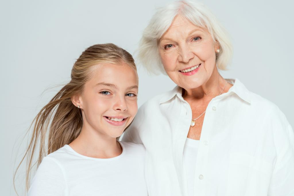 nieta sonriente y abuela mirando a la cámara aislada en gris
  - Foto, imagen