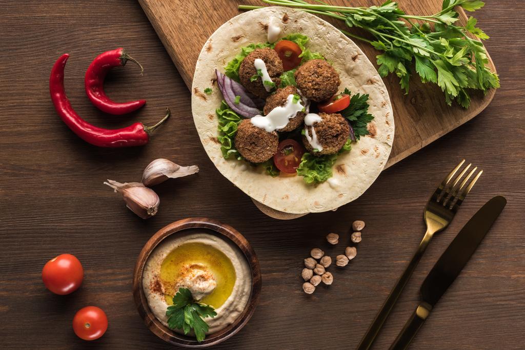 vue de dessus de falafel avec légumes sur pita près de couverts, épices et houmous sur table en bois près des épices
 - Photo, image