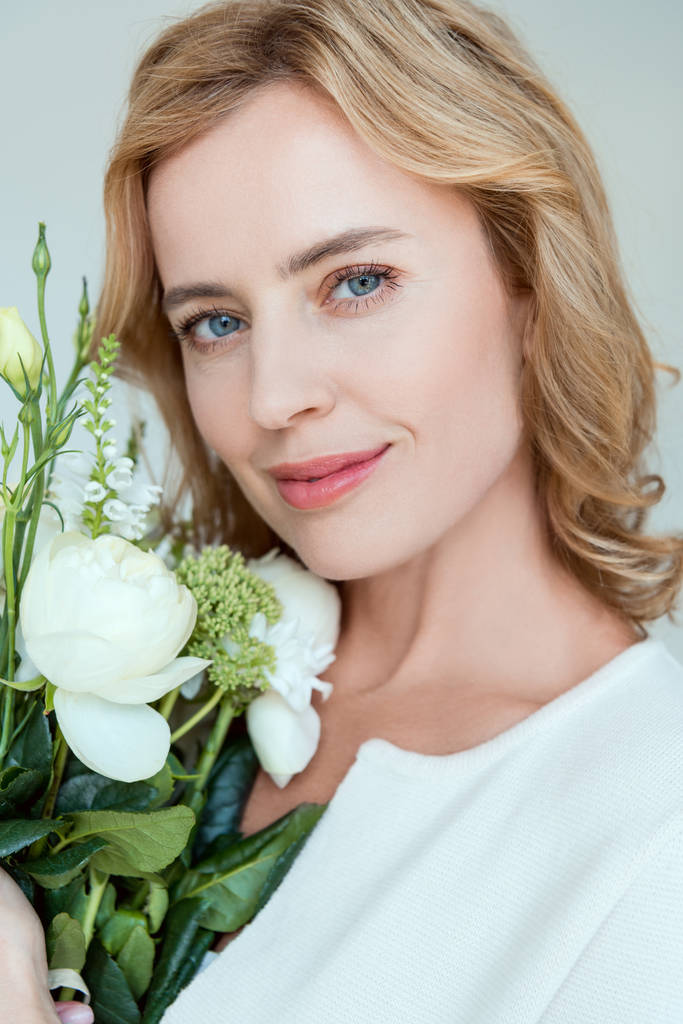 smiling and attractive woman with bouquet looking at camera isolated on grey - Photo, Image