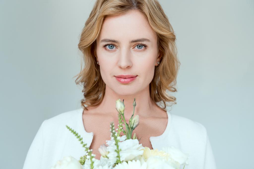 attraktive Frau mit Blumenstrauß blickt vereinzelt in die Kamera auf grau - Foto, Bild