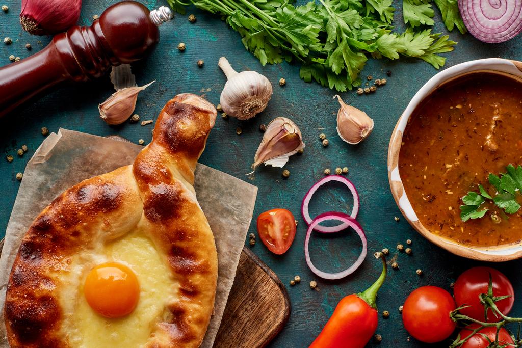 Top kilátás leves kharcho és adjarian khachapuri fűszerek és zöldségek texturált zöld háttér - Fotó, kép