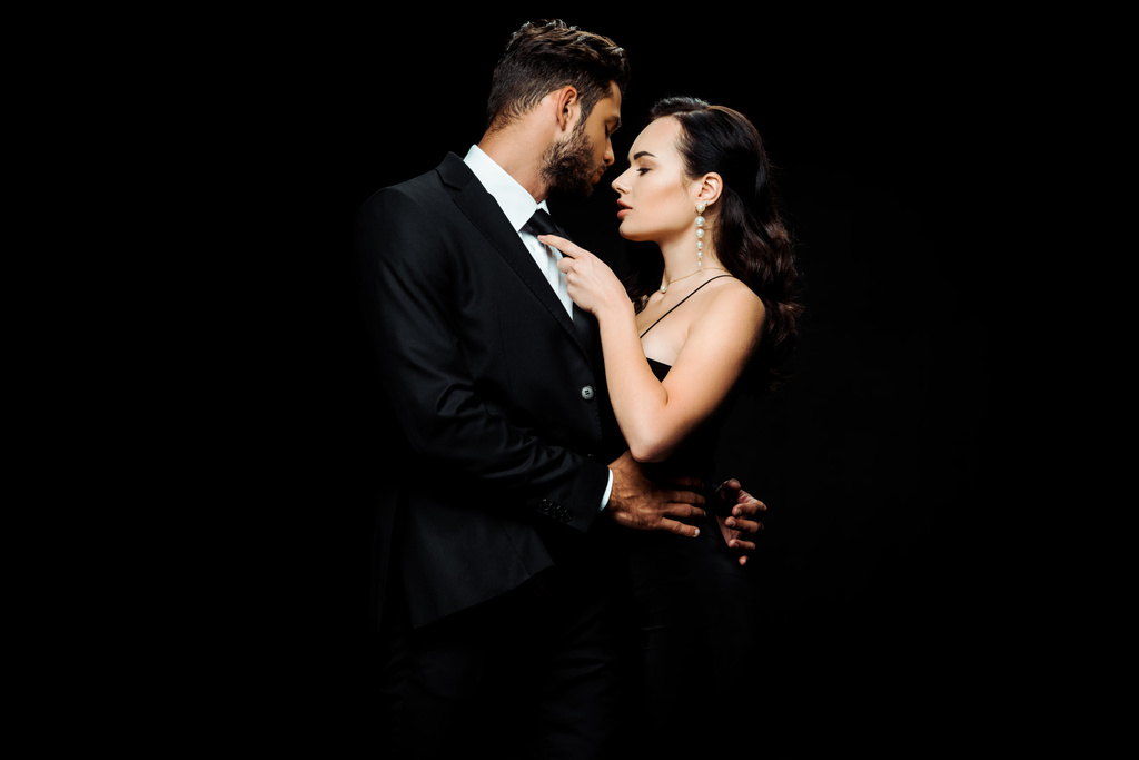 attractive woman in dress hugging boyfriend in suit isolated on black  - Photo, Image