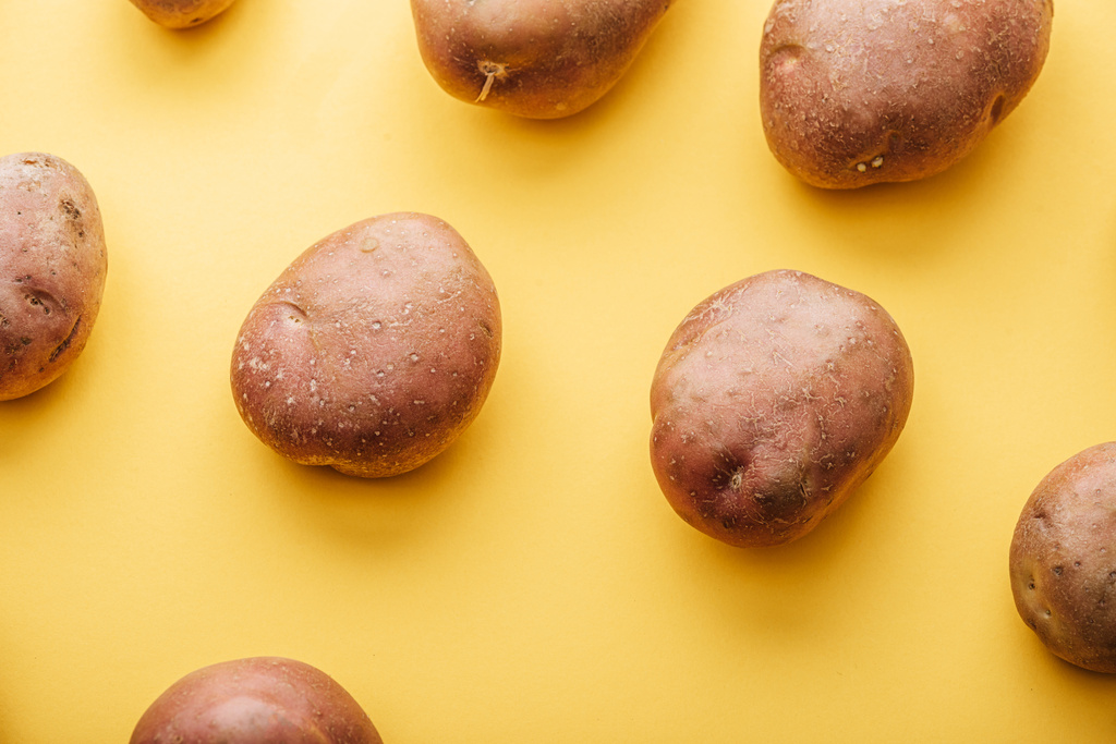 patroon van rauwe hele verse aardappelen op gele achtergrond - Foto, afbeelding