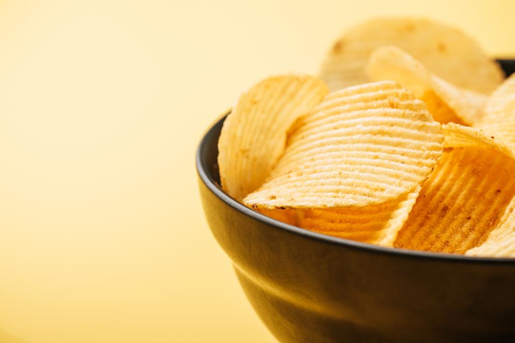 Nahaufnahme von köstlichen knusprigen Kartoffelchips in Schüssel auf gelbem Hintergrund - Foto, Bild
