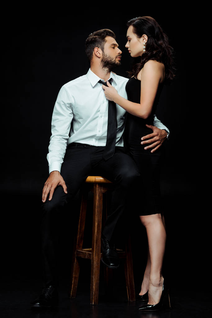 beautiful woman looking at bearded man sitting on chair isolated on black  - Photo, Image