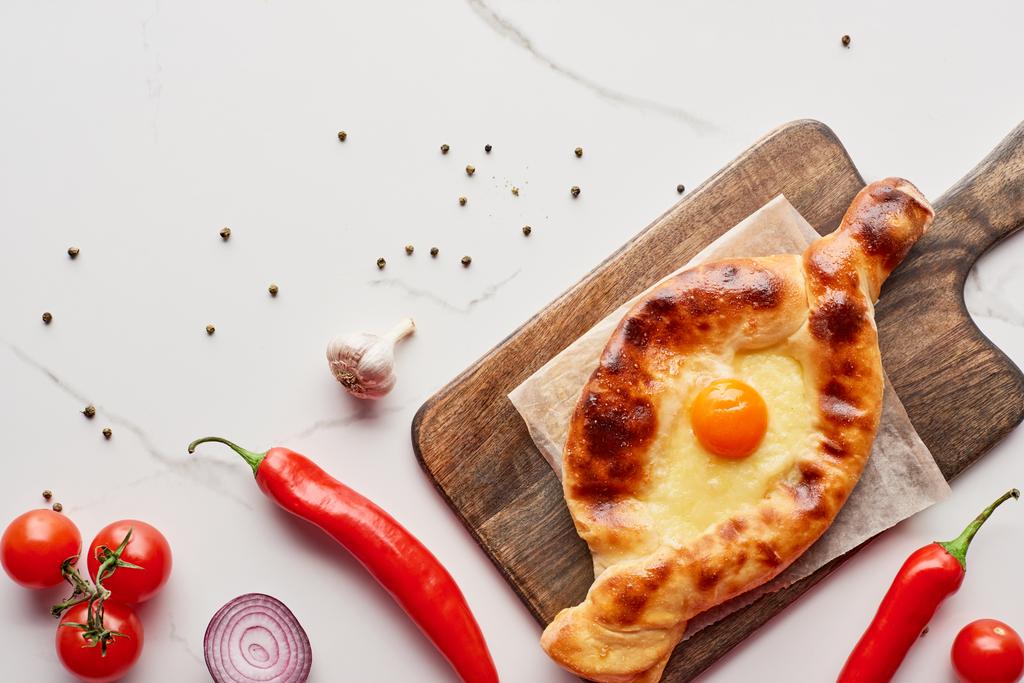 Top view of adjarian khachapuri on cutting board with vegetables on marble texture - Photo, Image