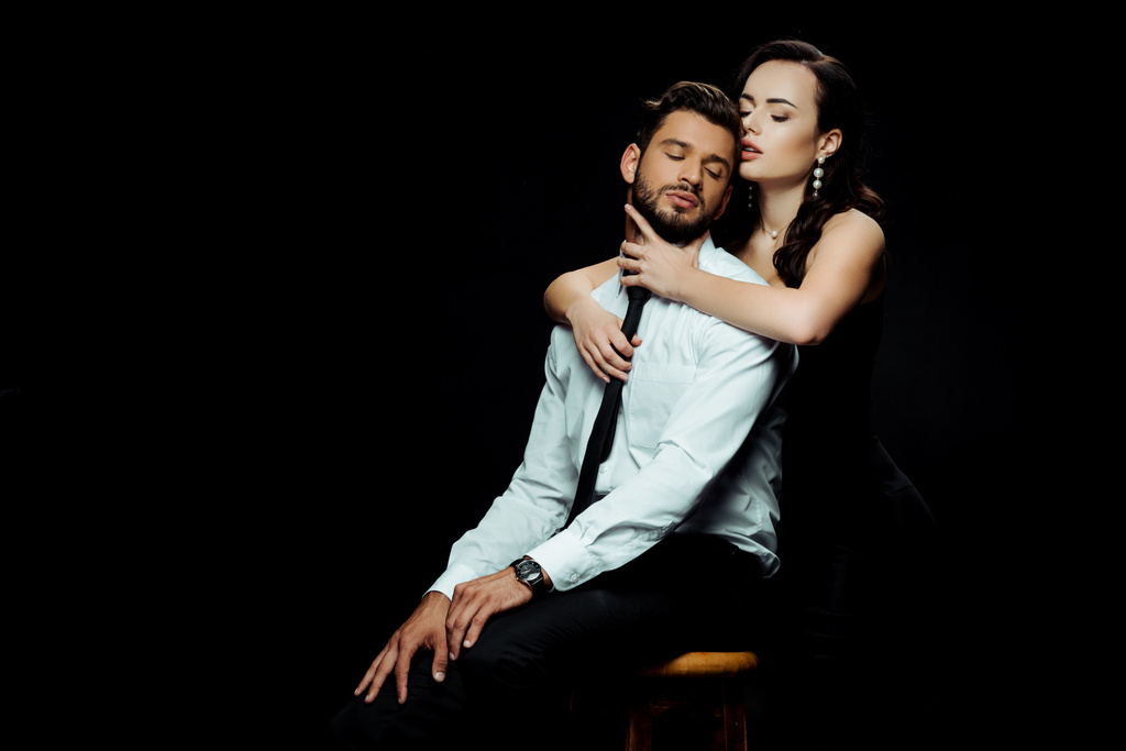 beautiful woman hugging bearded man sitting on chair isolated on black  - Photo, Image