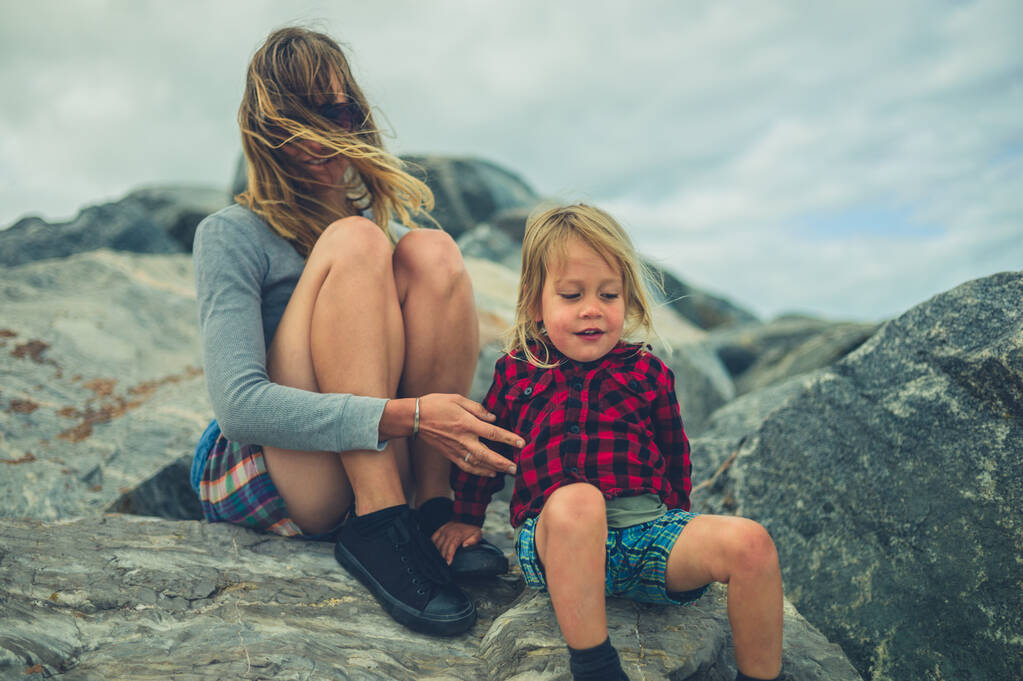 若い母親と彼女の小さな幼児が岩の上に座っている - 写真・画像