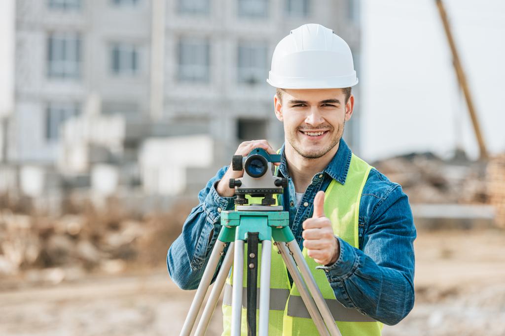 Surveyor with digital level smiling at camera and showing thumb up gesture - Photo, Image