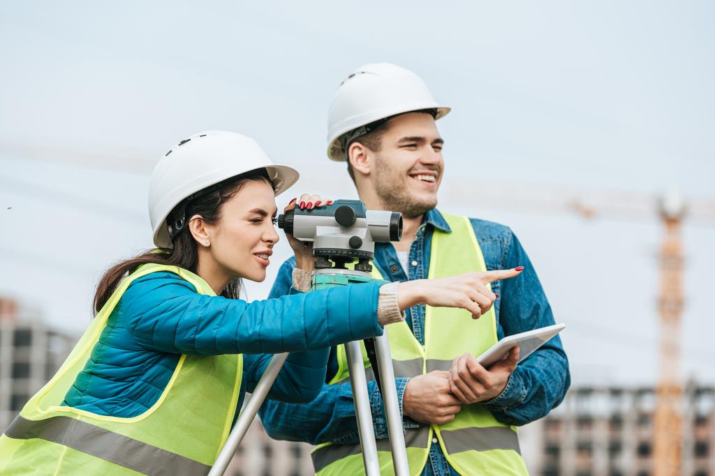 Surveyor looking through digital level and pointing away to colleague with tablet - Photo, Image