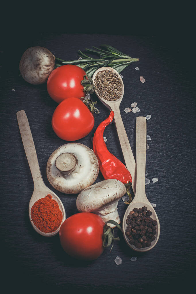 Legumes frescos, tomates e cogumelos com especiarias diferentes em um fundo preto
 - Foto, Imagem