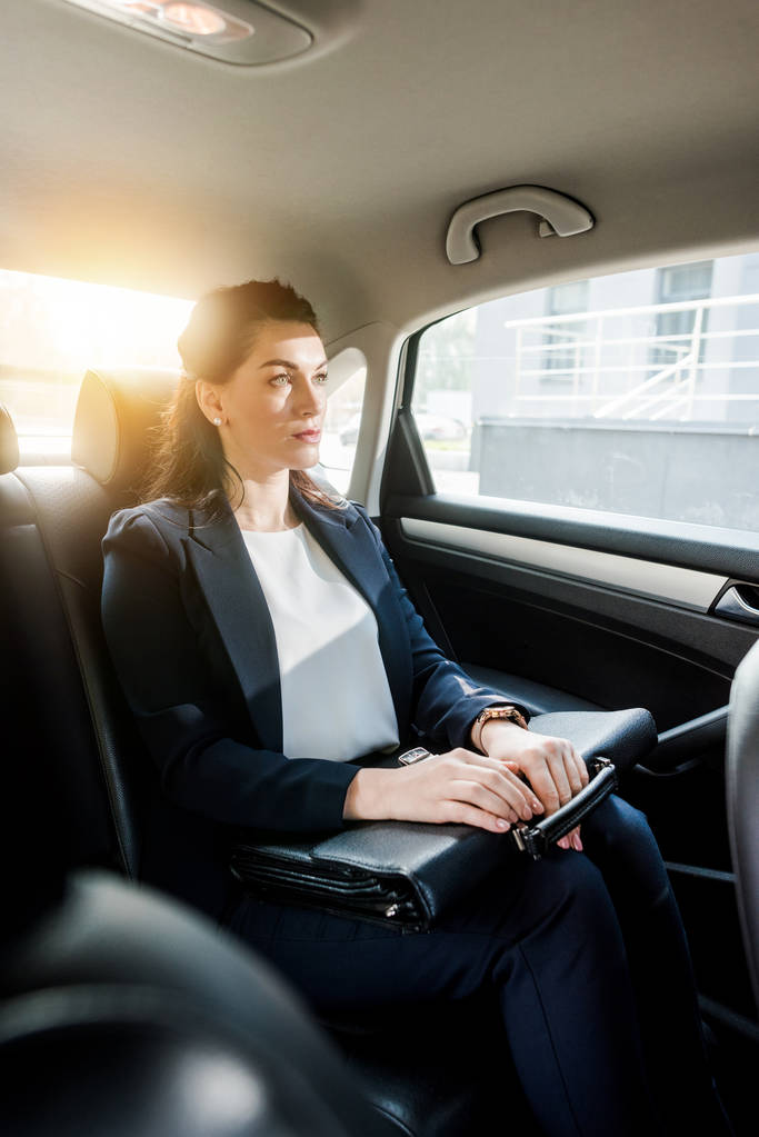 selective focus of beautiful ambassador holding briefcase while sitting in car  - Photo, Image
