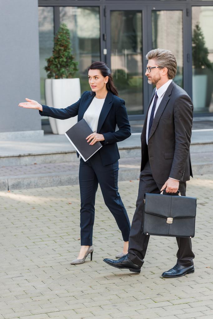 diplomata atraente apontando com a mão enquanto caminhava com o homem de óculos
  - Foto, Imagem