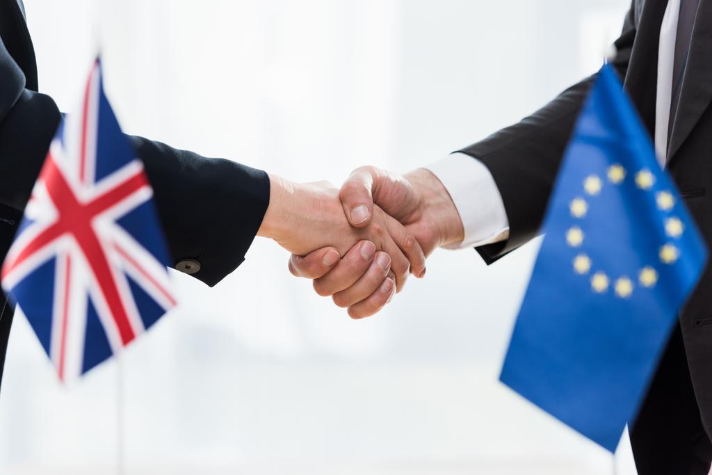 ostříhaný pohled na diplomaty, jak si podávají ruce poblíž Evropské unie a vlajek sjednoceného království  - Fotografie, Obrázek