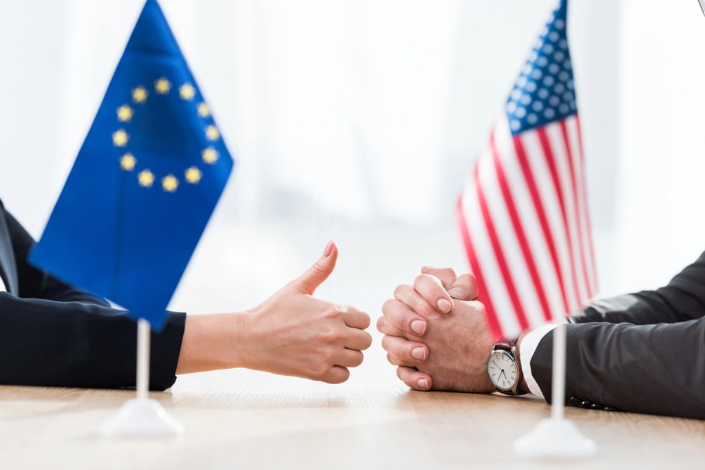 vista cortada de diplomata da união europeia mostrando polegar para cima perto embaixador dos EUA sentado com as mãos apertadas
  - Foto, Imagem