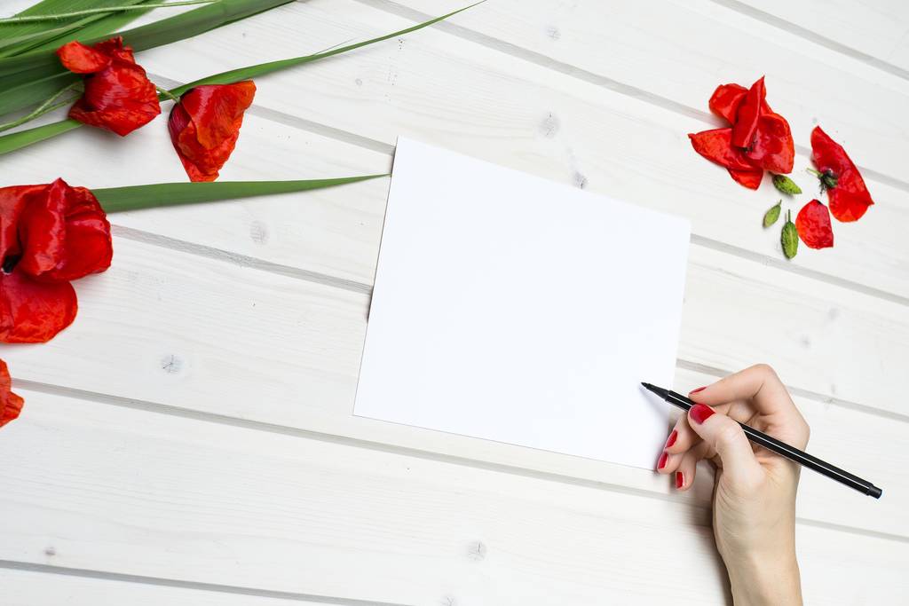 木製の表面に赤いチューリップの花びらの近くに黒いペンで白い紙に描く人の高い角度のショット - 写真・画像
