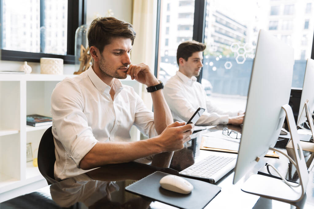 Immagine di due uomini d'affari seduti alla scrivania e con smartpho
 - Foto, immagini