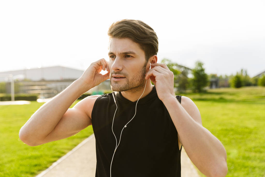 Kuva nuoresta miehestä työskentelemässä kuulokkeiden kanssa ja juoksemassa vihreässä puistossa ulkona aamulla
 - Valokuva, kuva