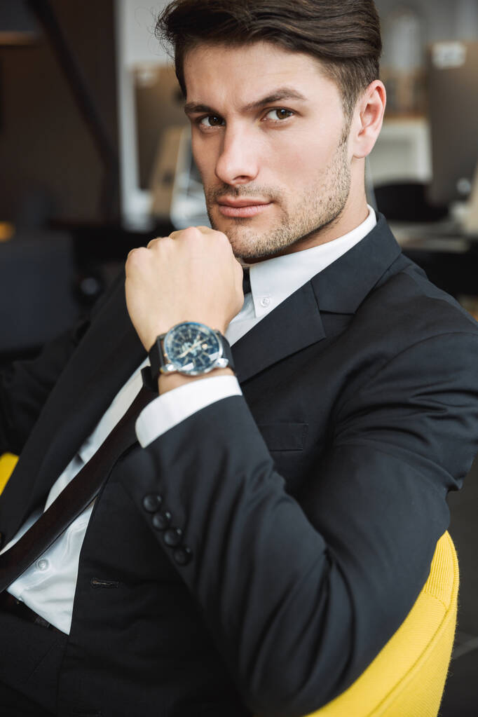 Portrait of masculine young businessman wearing wristwatch sitti - Photo, Image