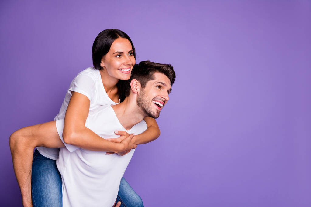 Tourné photo de mignon joyeux beau couple élégant à la mode de personnes souriant dentellement fille piggyback chevauchant son petit ami regarder espace vide isolé couleur violet pastel fond
 - Photo, image