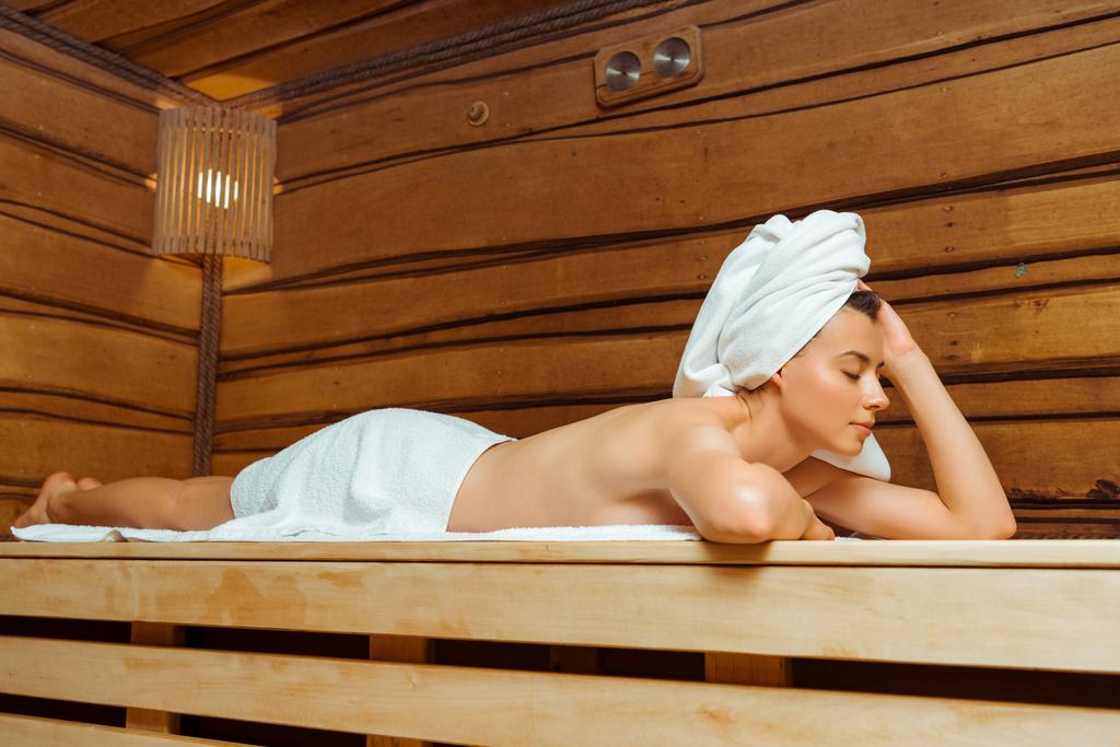 attraktive Frau in Handtüchern mit geschlossenen Augen in der Sauna liegend  - Foto, Bild