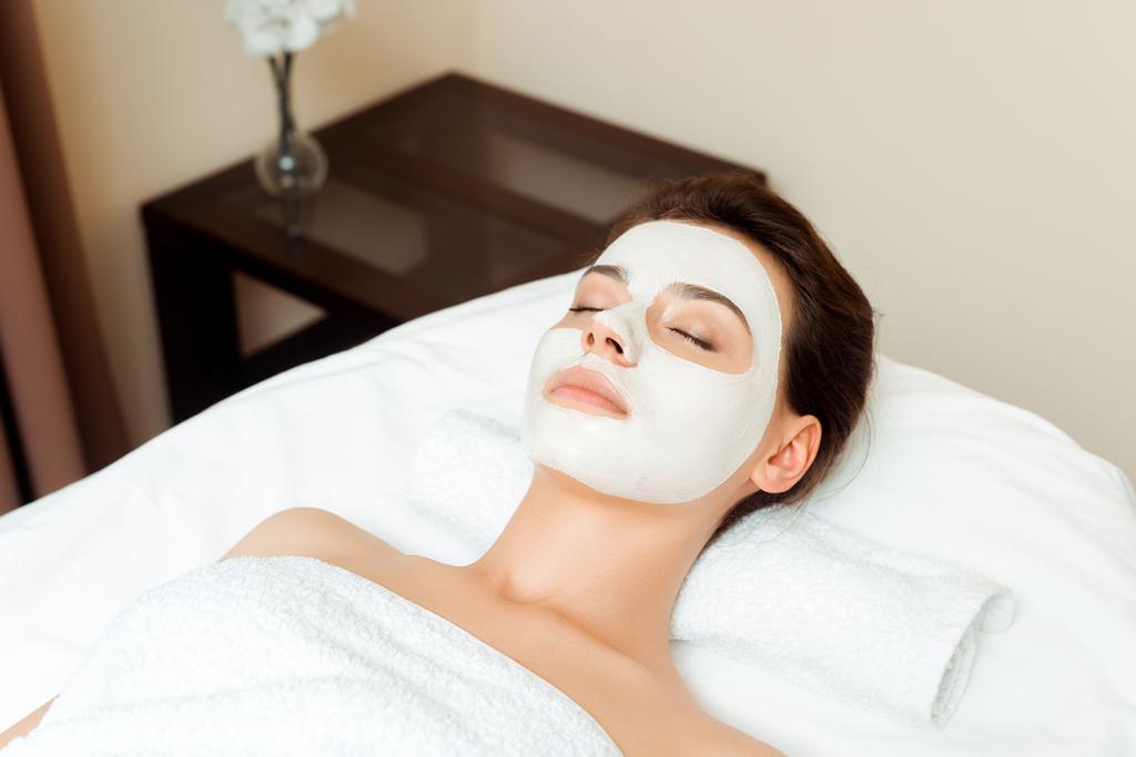 vista ad alto angolo di donna attraente con maschera sul viso sdraiato sul tavolo da massaggio in spa
  - Foto, immagini