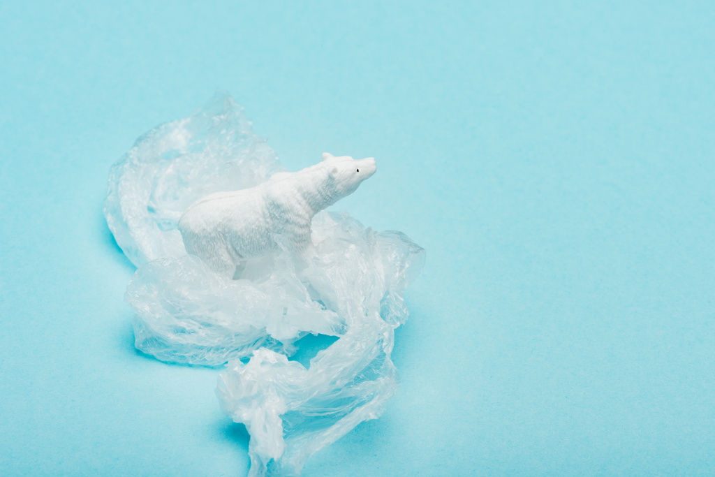 IJsbeer op plastic zak op blauwe achtergrond, dierenwelzijnsconcept - Foto, afbeelding
