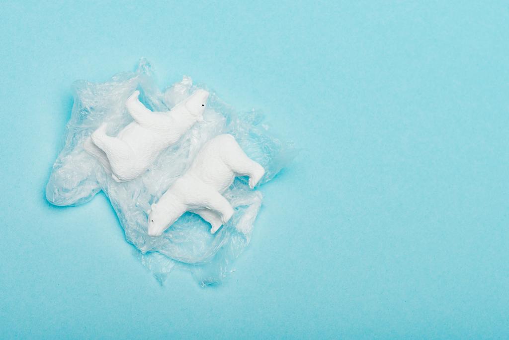 Top view of toy polar bears on polyethylene bag on blue background, environmental pollution concept - Photo, Image