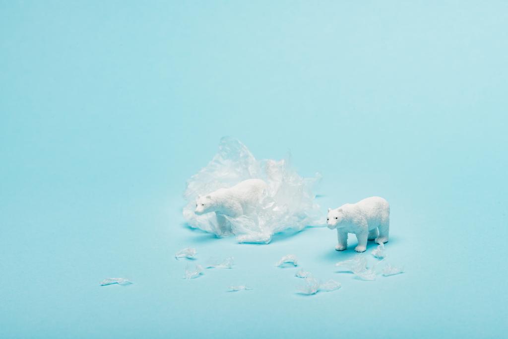 Toy polar bears with polyethylene trash on blue background, animal welfare concept - Photo, Image