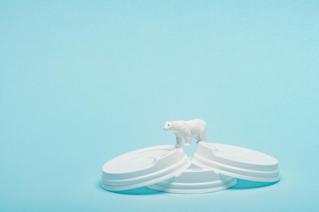 Toy polar bear on plastic coffee lids on blue background, animal welfare concept - Photo, Image
