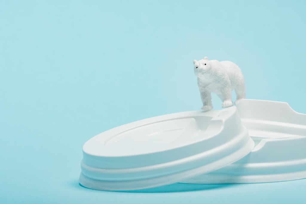 Mavi arka planda plastik kahve kapakları üzerine oyuncak kutup ayısı, ekolojik problem kavramı - Fotoğraf, Görsel