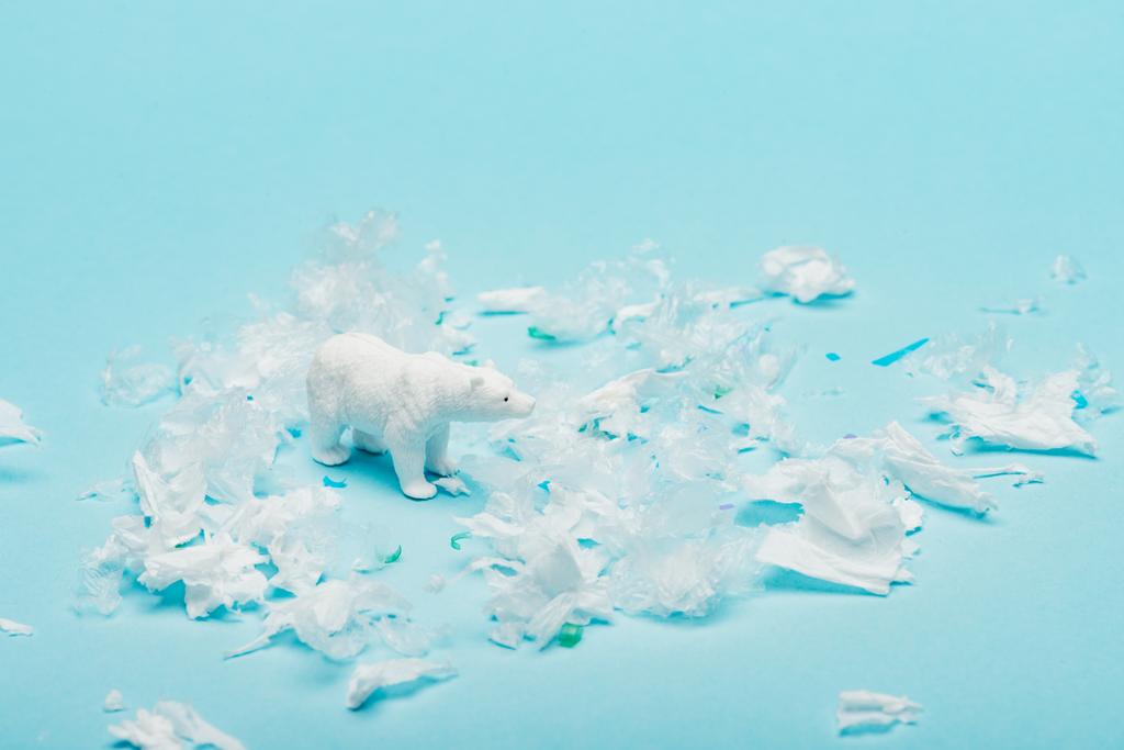 Toy polar bear with polyethylene and plastic garbage on blue background, animal welfare concept - Photo, Image